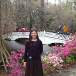 April Cassidy standing in front of a creek with a white bridge and azaleas blooming in the background