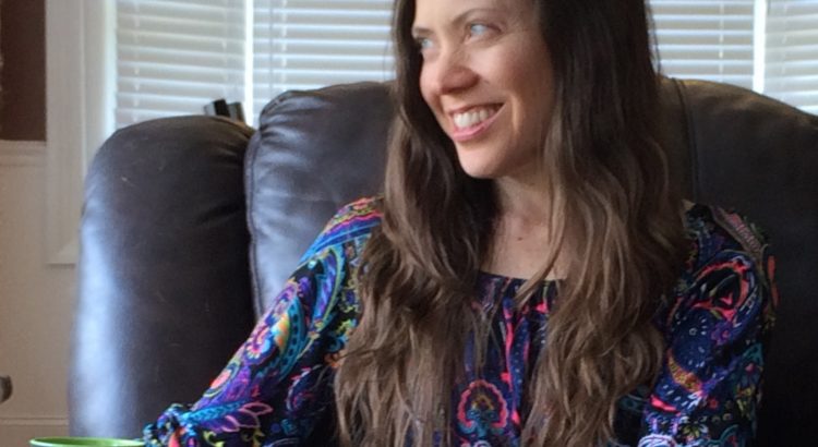 woman with long brown hair turning her head to the side and smiling while sitting on a brown leather couch