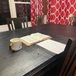 Open Bible, coffee mug, stack of paper on a dining room table for quiet time