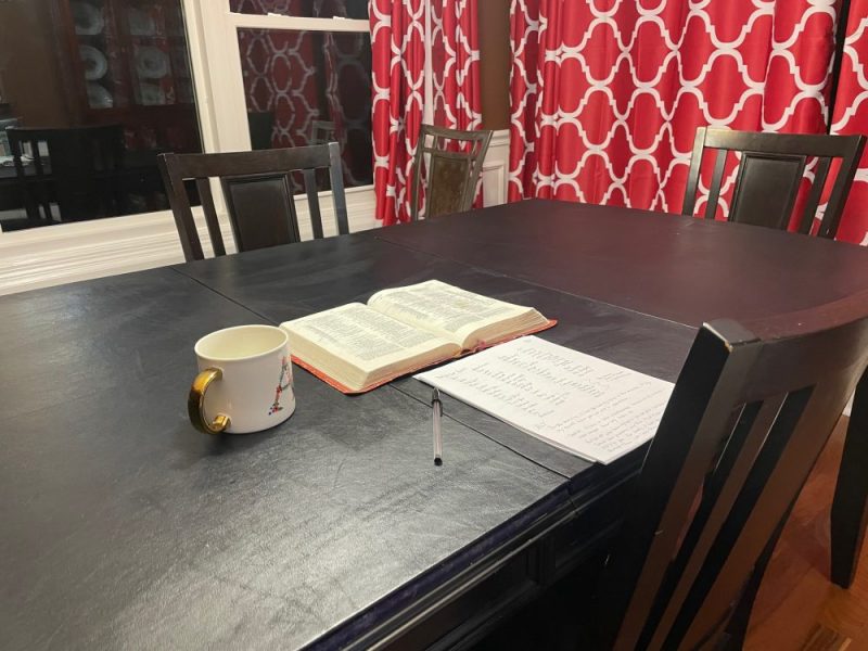 Open Bible, coffee mug, stack of paper on a dining room table for quiet time